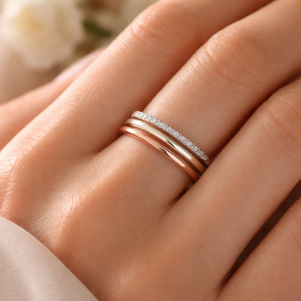 A photorealistic close‑up of three thin stackable rings—rose gold, white gold, and a diamond‑accented band—arranged on a woman's hand, soft natural light highlighting the metal tones, realistic style, appealing to women interested in fine Swiss jewellery.