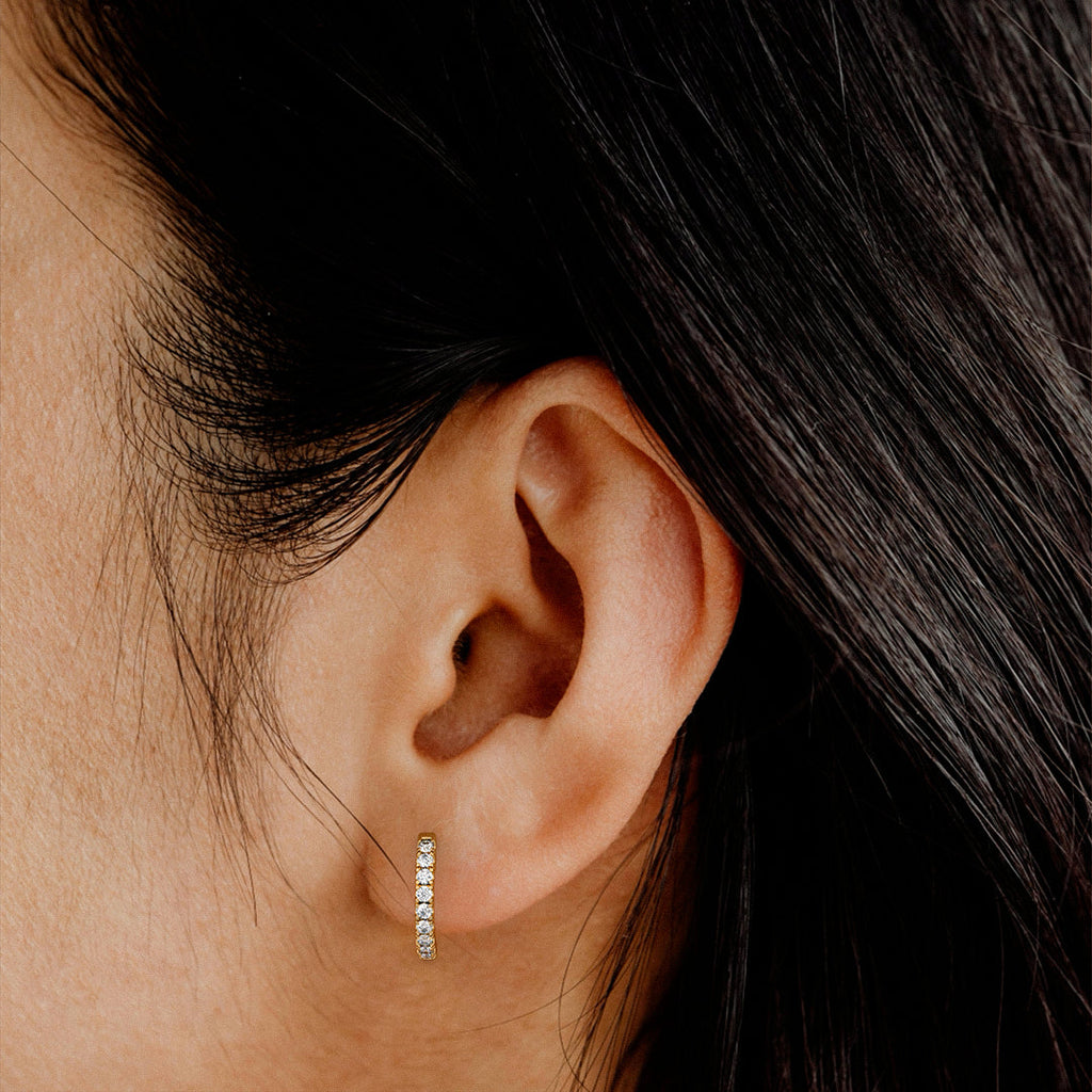 Close up of an ear wearing a small hoop earring with dark hair