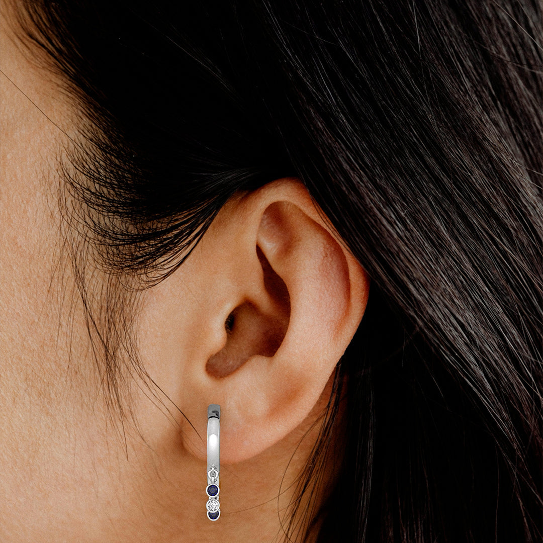 Close-up of an ear wearing a silver hoop earring with blue stones.