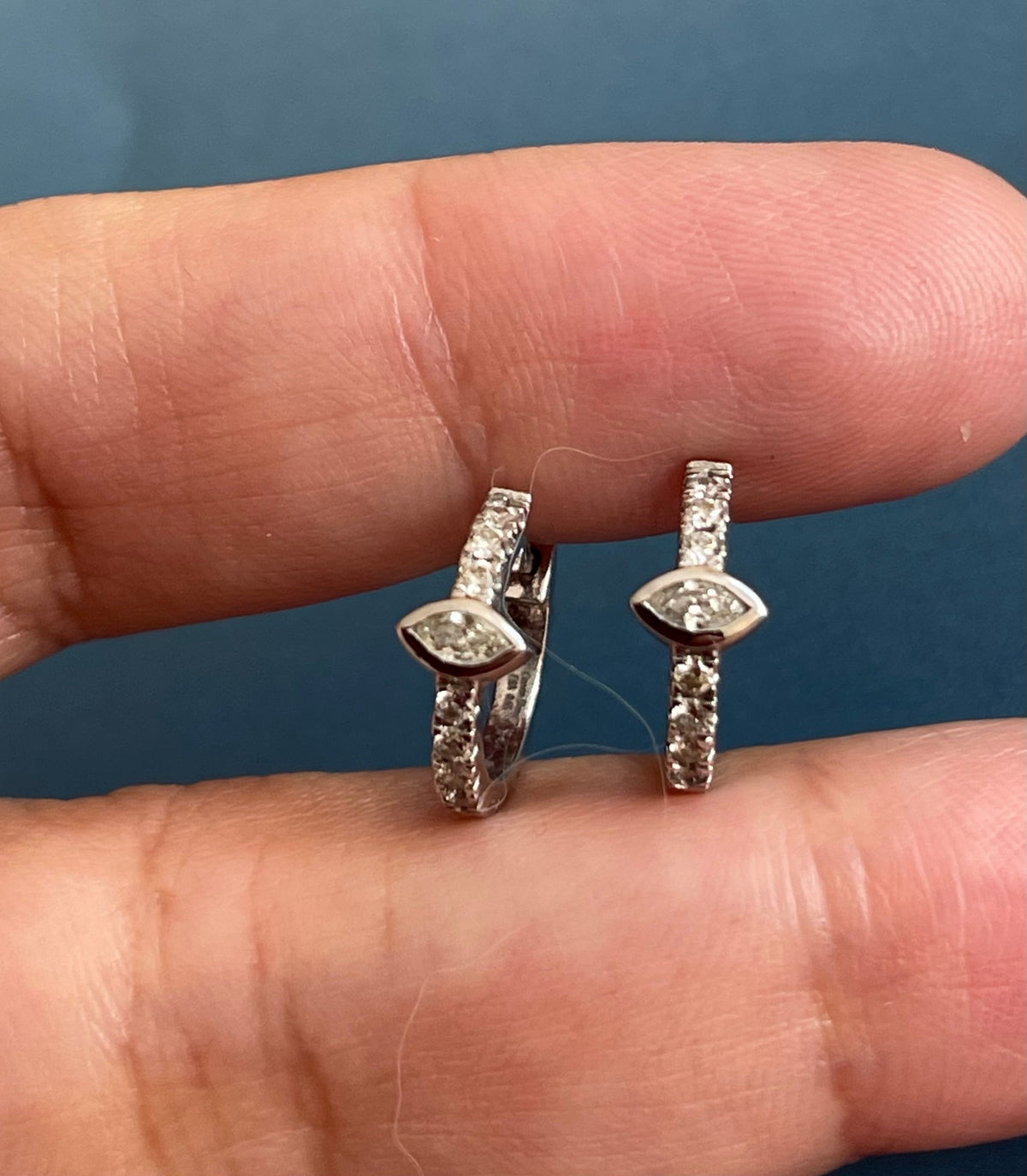 Two diamond stud earrings held between fingers against a blue background
