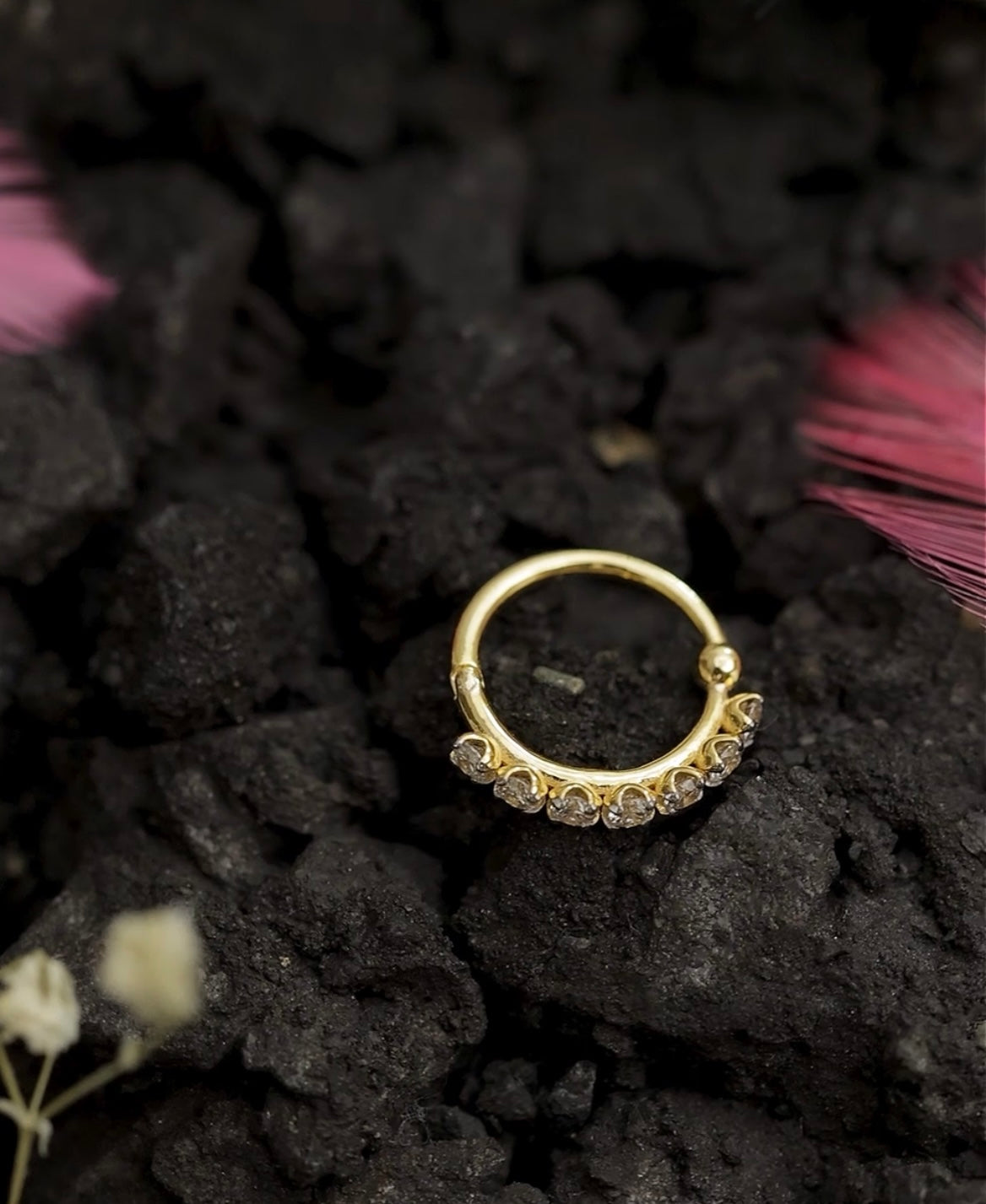 Gold nose stud with gemstones on a dark textured surface