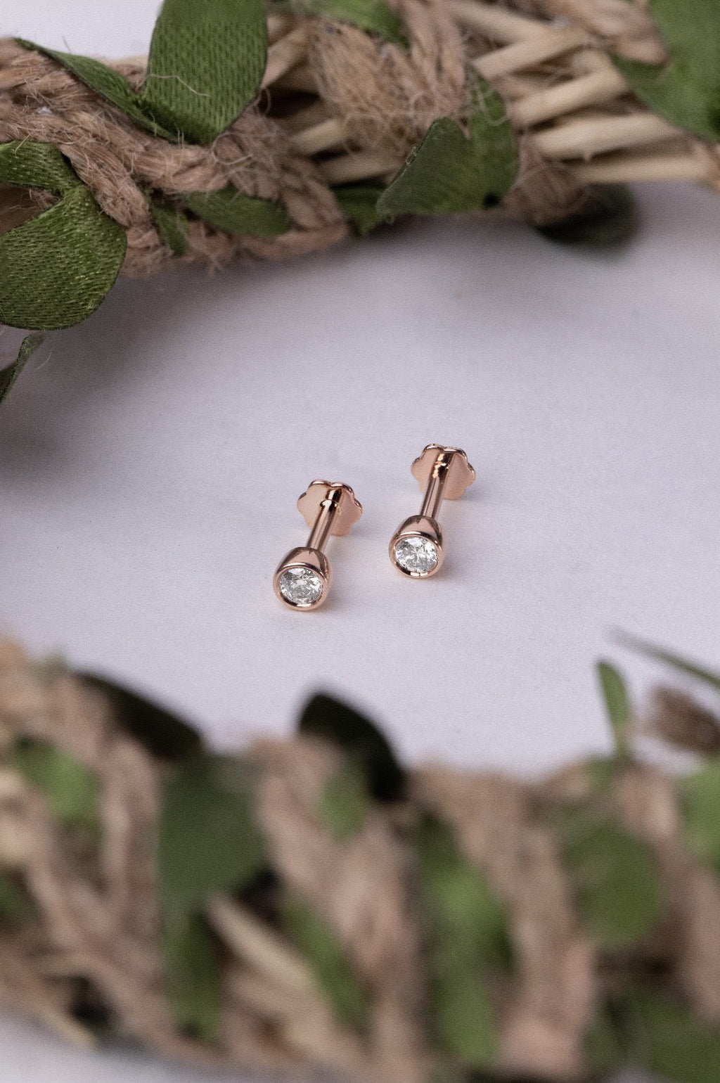 Rose gold nose stud gemstones on a white cushion with green leaves and brown twine.