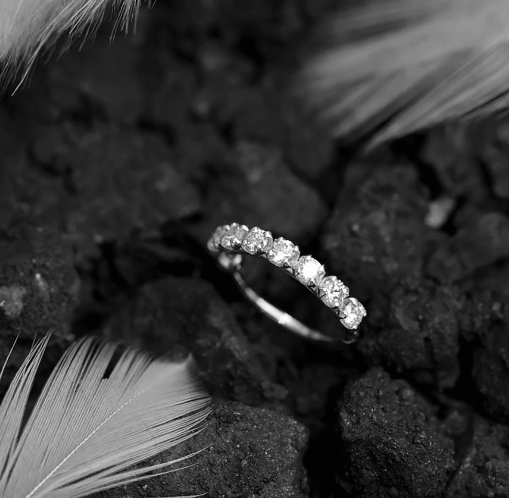 Silver ring with small diamonds on a dark textured surface with feathers