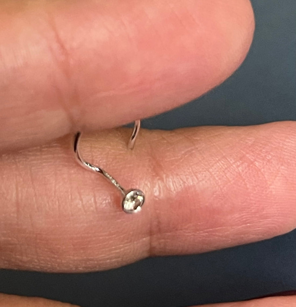 Silver ring with a small diamond on a finger against a dark background