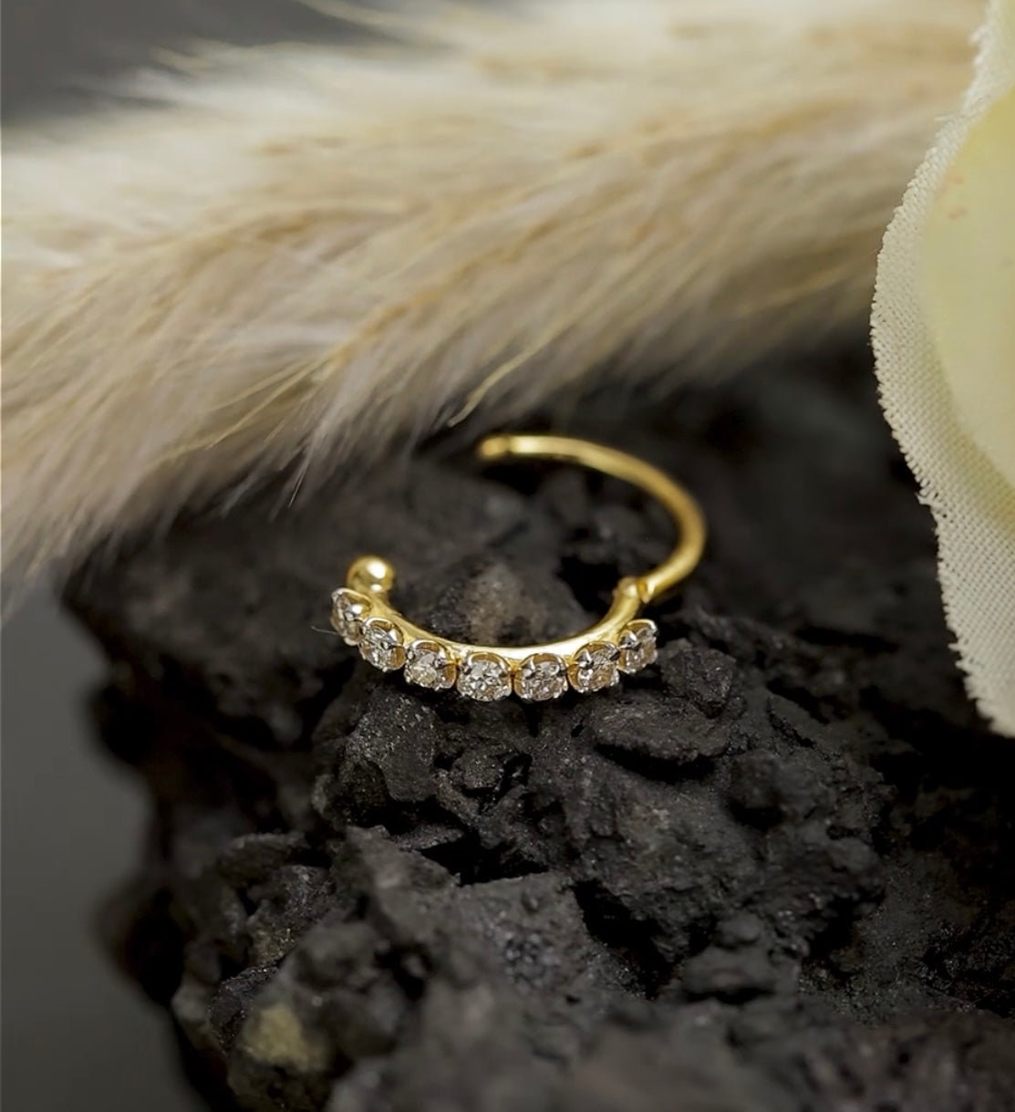 Gold hoop nose stud with small diamonds on a dark textured surface