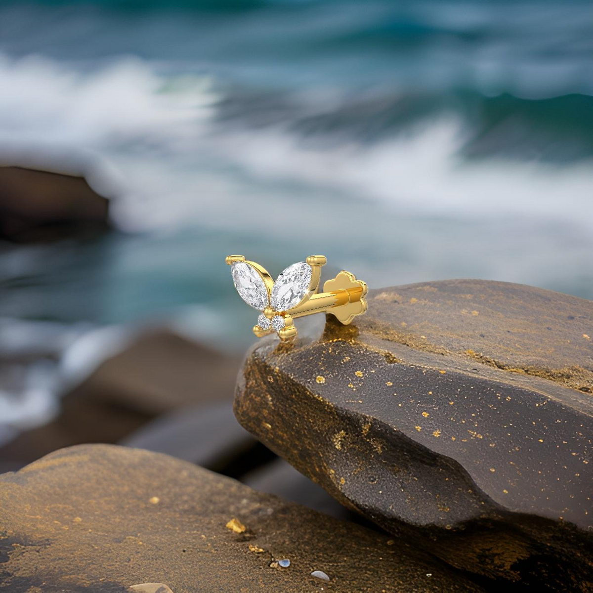 Gold bee-shaped nose stud with clear stones on a rock by the ocean